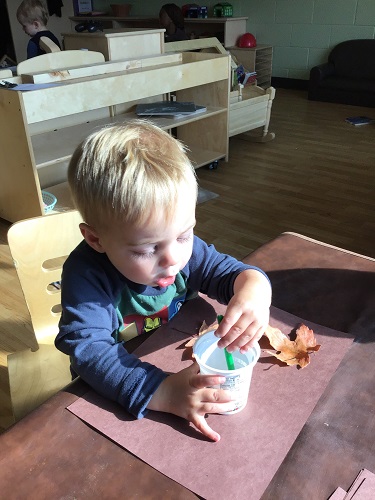 A child sitting at a table using glue to stick leaves onto a paper