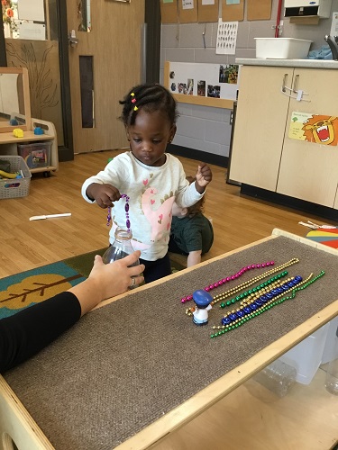 A child putting beads in and out of a plastic bottle