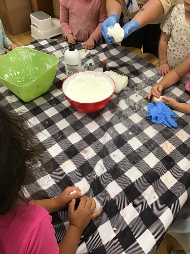 Children at a table mixing ingredients to make cloud dough