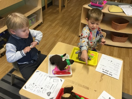 Two children sitting at a table using vet instruments to take care of stuffed animals