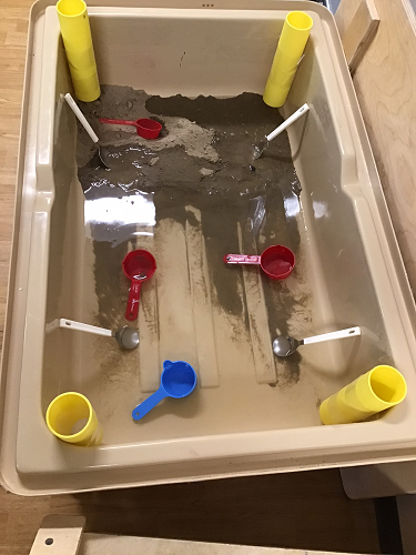 A sensory bin set up with sand, scoops and tubes