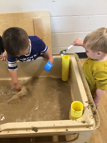 Two children playing in the sensory bin filled with muddy water