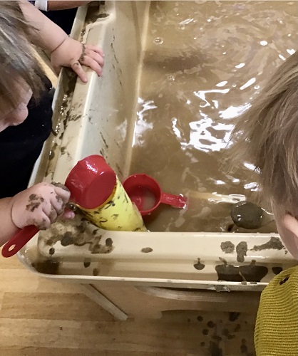 Two children scooping muddy water into tubes