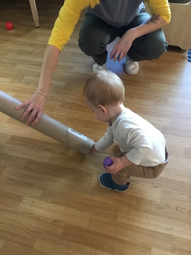 An infant reaching into the bottom of a cardboard tube