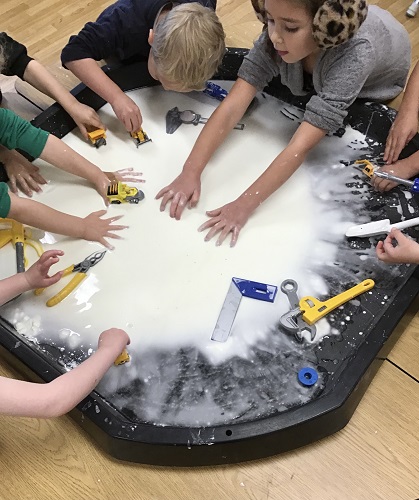 A group of children around a tuff tray filled with oobleck and tools