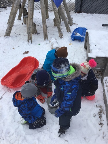 Children gathering around a pail, filling it with snow