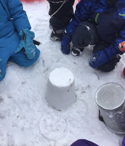 Children kneeling in the snow in front of a snow castle