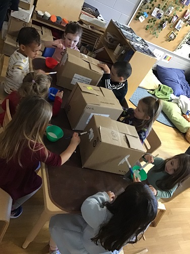 A group of children at a table painting big cardboard boxes