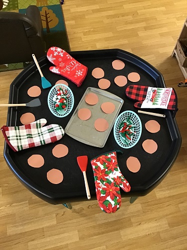 A tuff tray set up with oven mitts, baking tools and pretend cookies