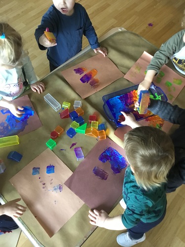 Children surrounding a table painting with plastic shapes