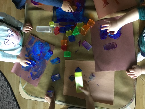 Children surrounding a table painting with plastic shapes