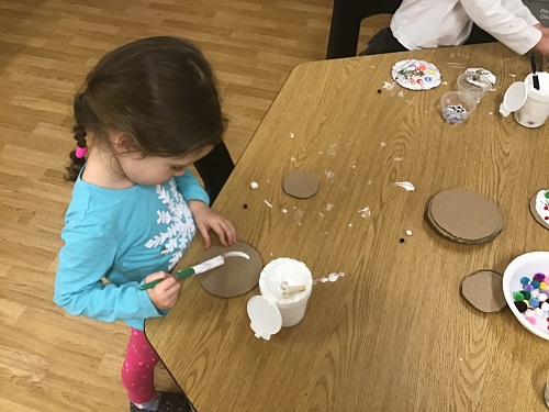 A child sitting at a table painting on a cardboard cirlce