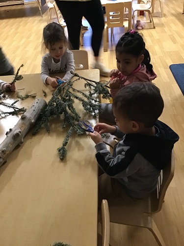 Children sitting at a table cutting pieces off a larger branch