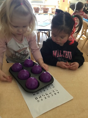 Two children at a table looking down at a muffin tin filled with balls