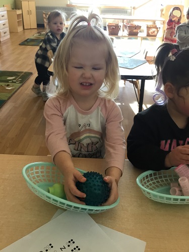 A child with her eyes closed feeling a ball on the tabe in front of her
