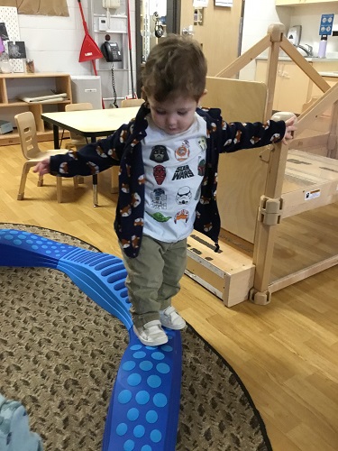 A child standing on the balance beam with his arm spread out