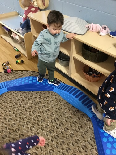 A child standing on the balance beam holding onto the shelf beside him