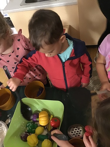 A child using a spoon to mix play food in a large bowl at the table