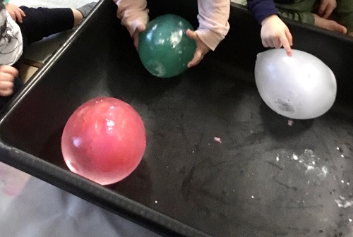 A child's hands trying to pick up a large ball of ice