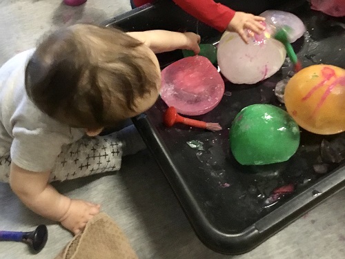 A child reaching into a large bin of frozen water balloons