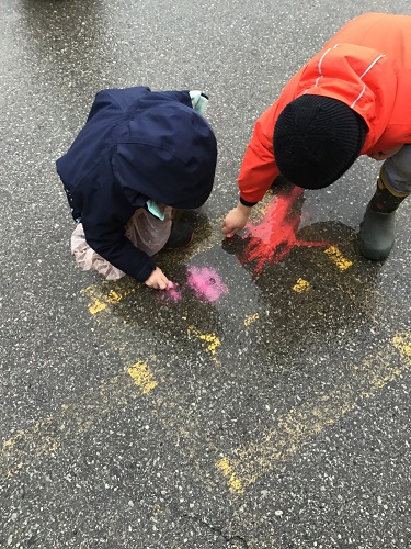 Two children beginning to colour with chalk on the pavement