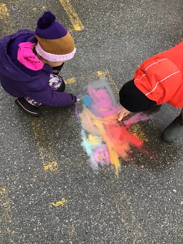 Two children colouring with chalk on the pavement