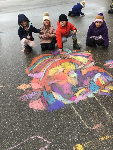 A group of children squatting beside a colourful chalk drawing on the pavement