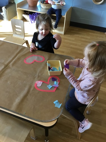 Two children sitting at a table working on the craft in front of them