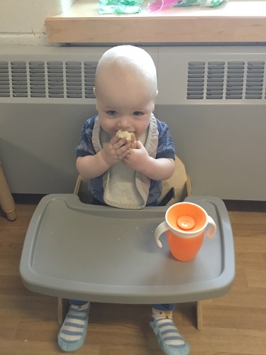 An infant sitting in a high chair tasting the bread they made