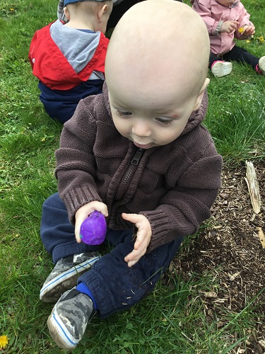 Infants sitting in the grass holding a rock