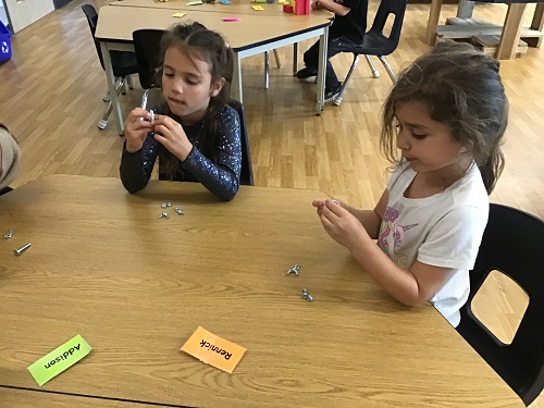 Two children at a table making their creations for Father's Day out of nuts and bolts