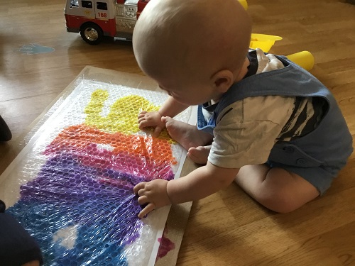 An infant touching bubble wrap covering different shades of paint