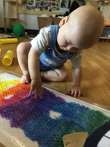 An infant touching bubble wrap covering different shades of paint