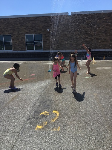 Children on the black top running through the sprinkler