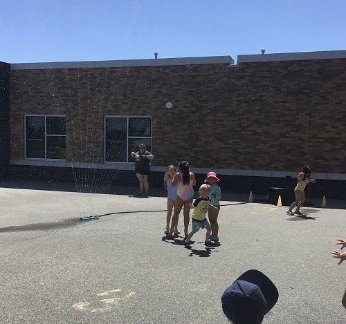 Children on the black top running through the sprinkler