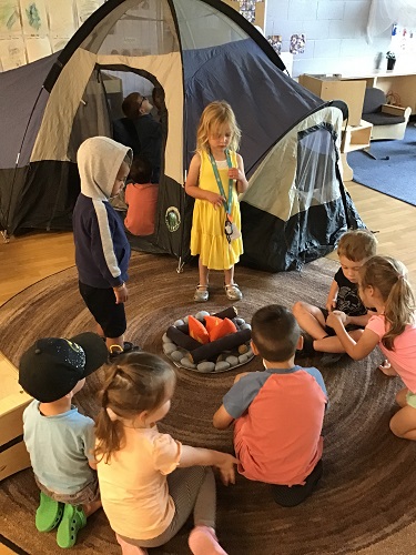 Children sitting around a pretend camp fire in front of a tent