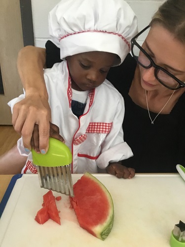 An educator helping an infant cut up fruit with child-safe knives