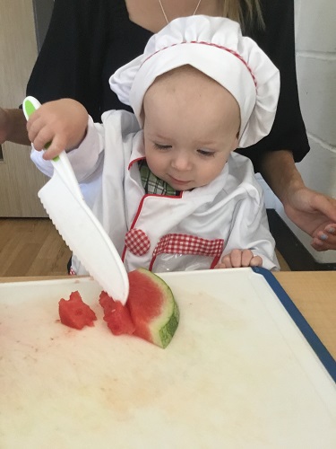 An educator helping an infant cut up fruit with child-safe knives