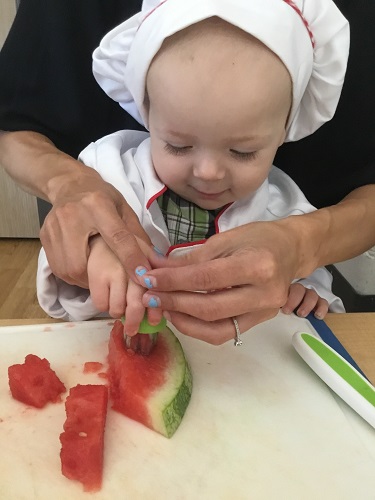 An educator helping an infant cut up fruit with child-safe knives