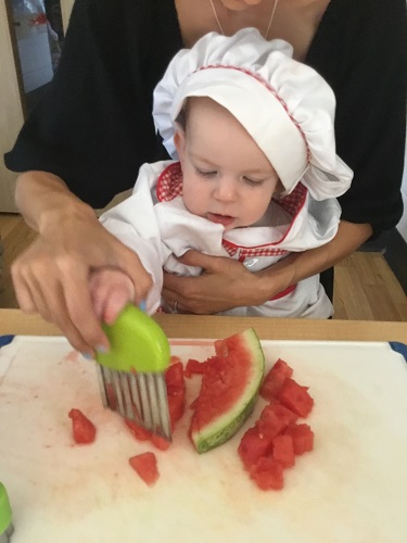 An educator helping an infant cut up fruit with child-safe knives