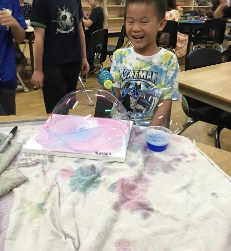 A child sitting at a table with a large bubble sitting on a canvas in front of him