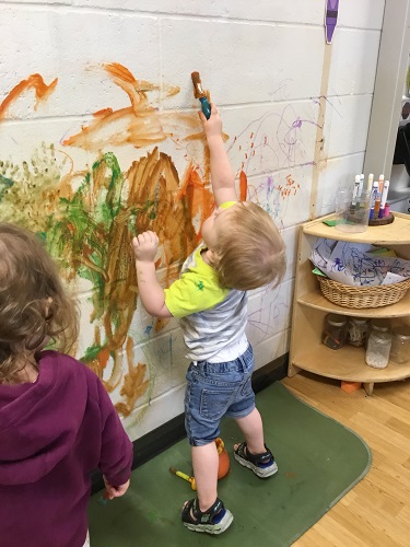 A child reaching up high to paint on a wall