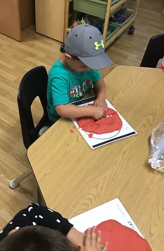 A child sitting at a table squishing playdough into a circle to create a pizza