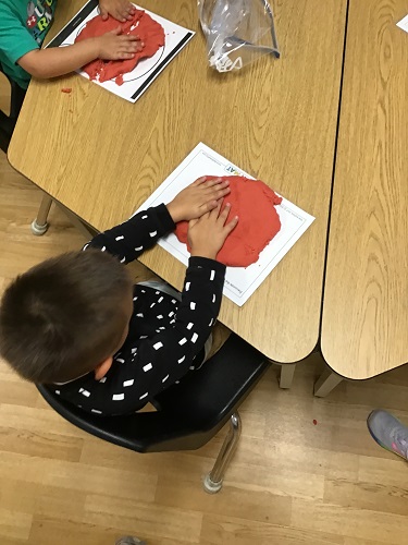 A child at a table squishing playdough into a flat circle