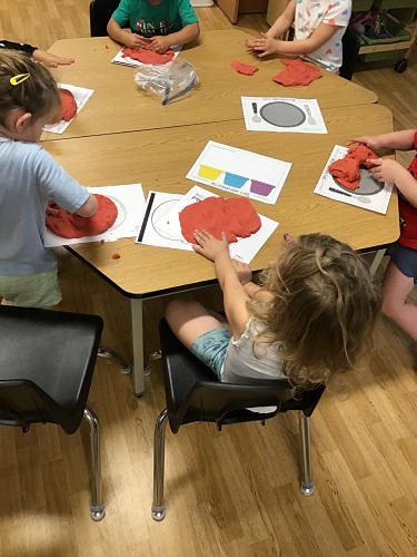 Children sitting around a table turning playdough into pizzas