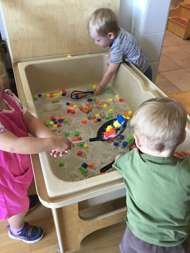 Children using large utensils to scoop foam blocks in a sensory bin filled with water