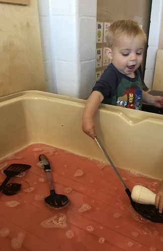 A child using a large spoon to scoop water in a sensory bin