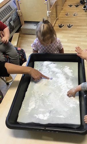 Children and an educator at a sensory bin pointing to the foam 