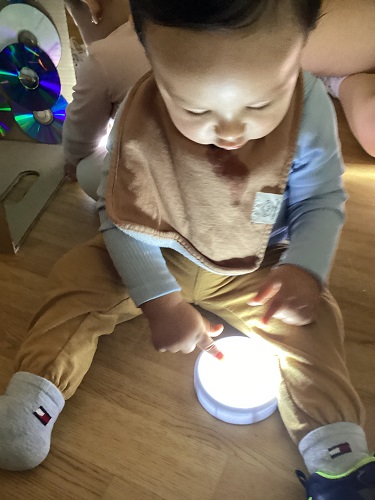 A child sitting on the floor using a finger to point at a puck light