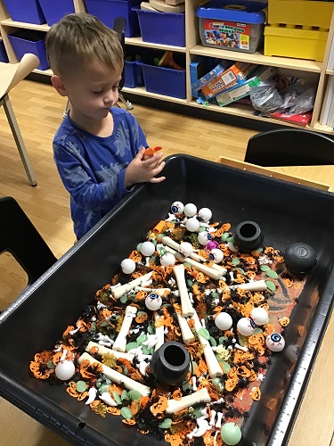 A child playing in a sensory bin filled with Halloween themed items